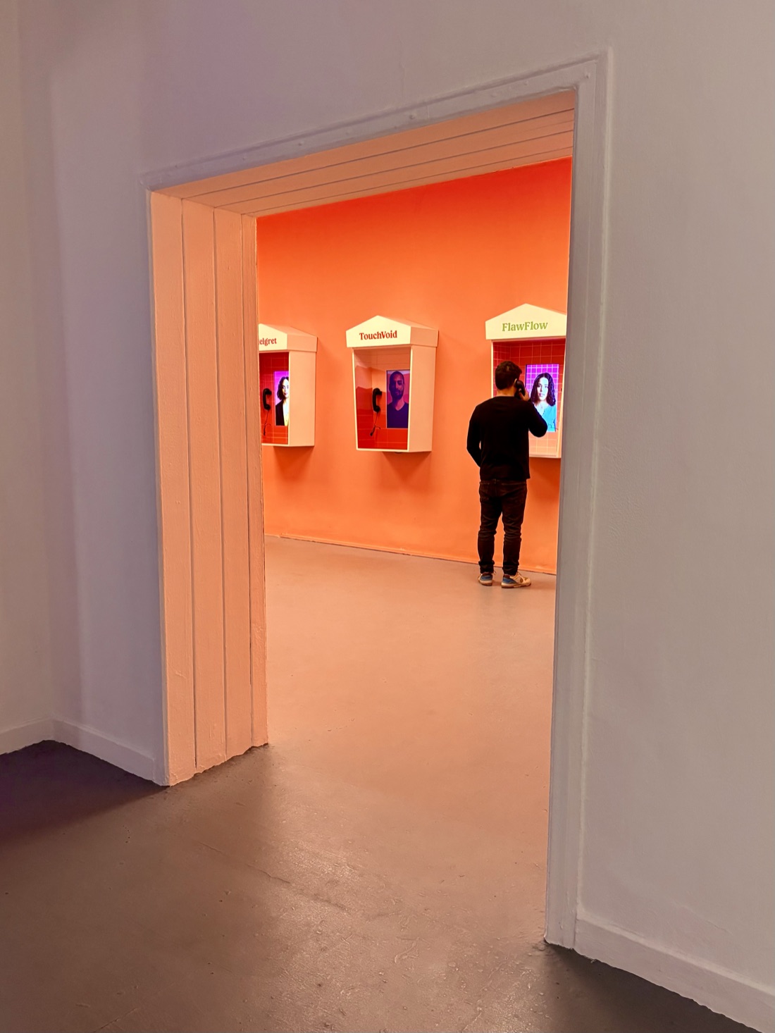 A doorway view into the glowing exhibition room, a visitor at the FlawFlow booth