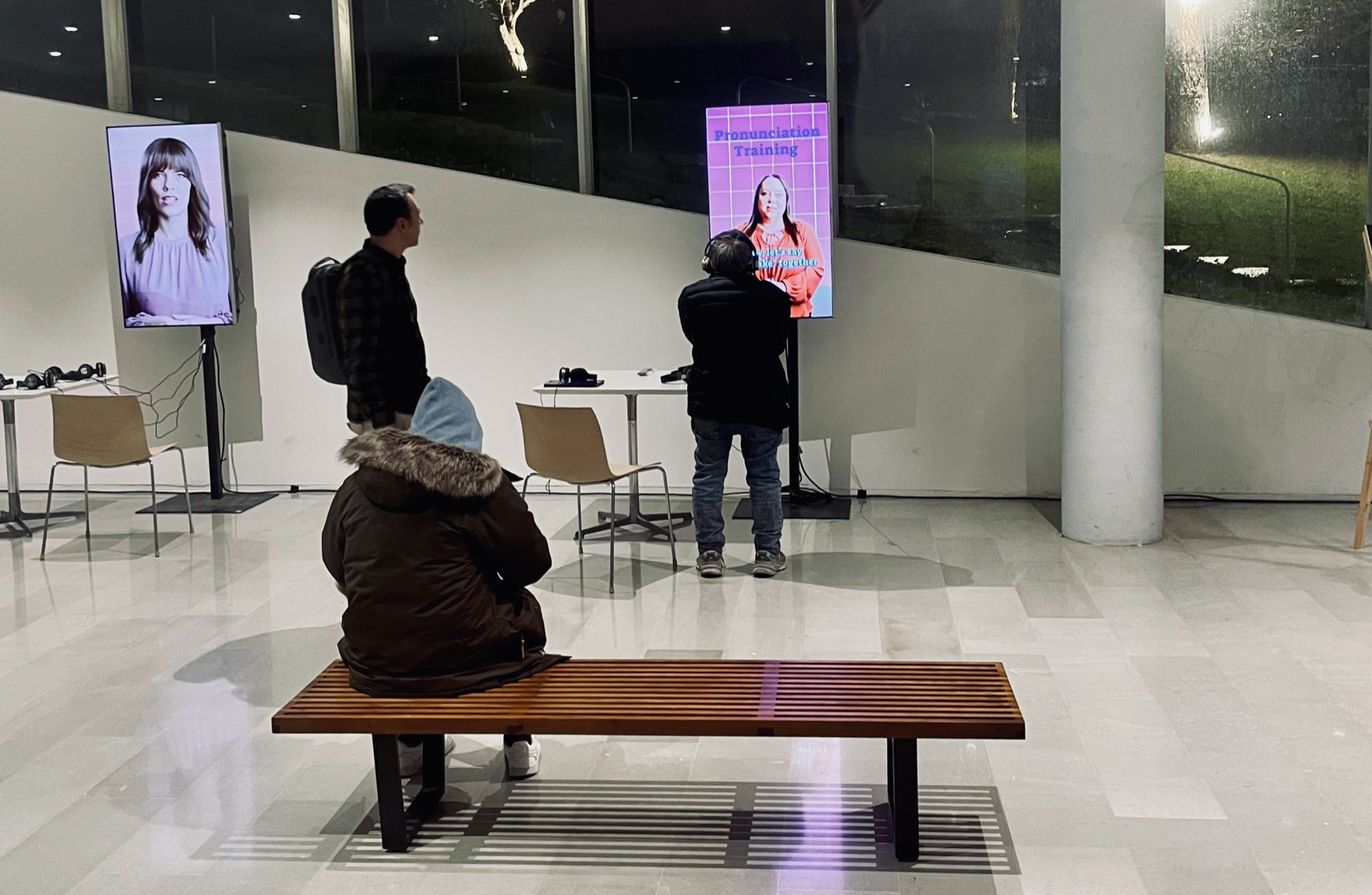 The Van Leer festival hall at night: visitors on a bench and at vertical screens showing the synthetic instructors