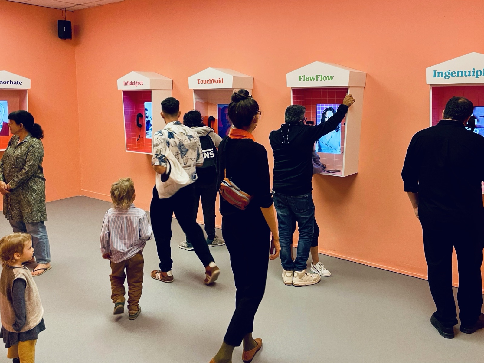 Visitors and children moving between the emotion booths on the coral gallery wall